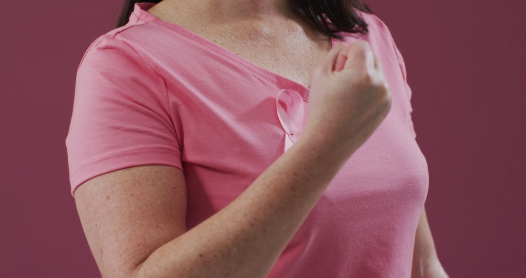 Mid section of a woman with pink ribbon on her chest clenching her fist against pink background - Free Images, Stock Photos and Pictures on Pikwizard.com