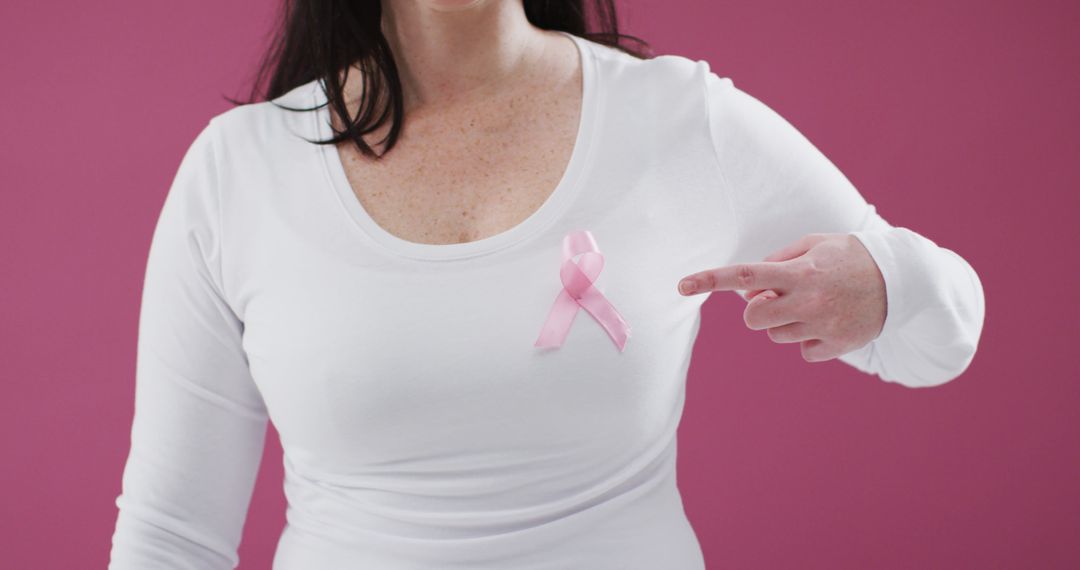 Woman Pointing to Pink Ribbon on White Shirt Against Pink Background - Free Images, Stock Photos and Pictures on Pikwizard.com