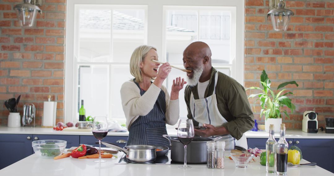 Biracial senior couple wearing aprons tasting food while cooking in the kitchen at home - Free Images, Stock Photos and Pictures on Pikwizard.com