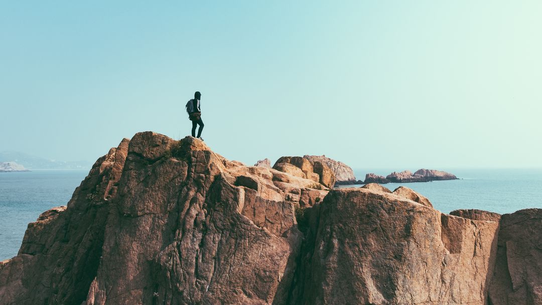Adventurer Standing on Rugged Coastal Cliff Overlooking Sea