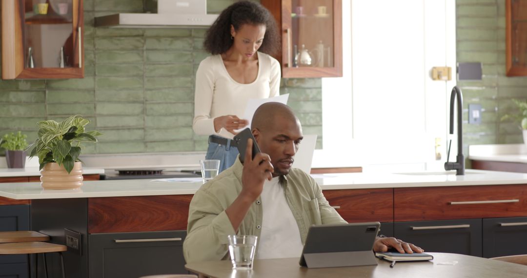 Man Multitasking with Smartphone and Tablet in Kitchen