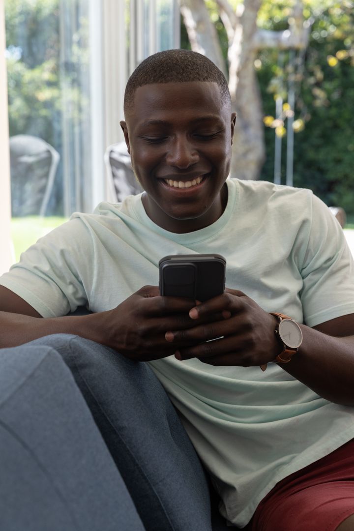 Man Smiling While Checking Smartphone Relaxing on Sofa