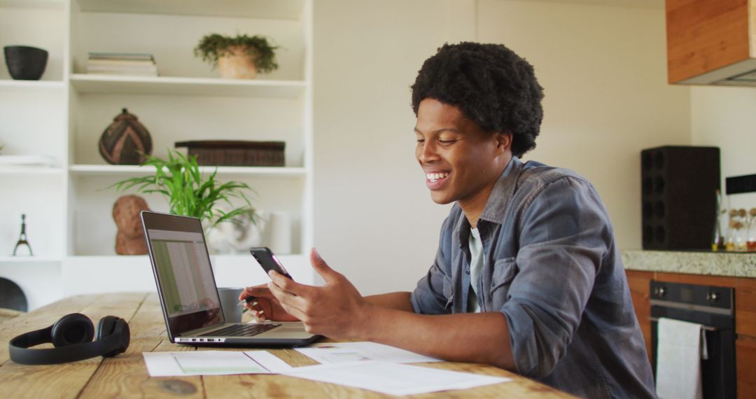 Remote Working African American Man Smiling at Laptop Using Phone
