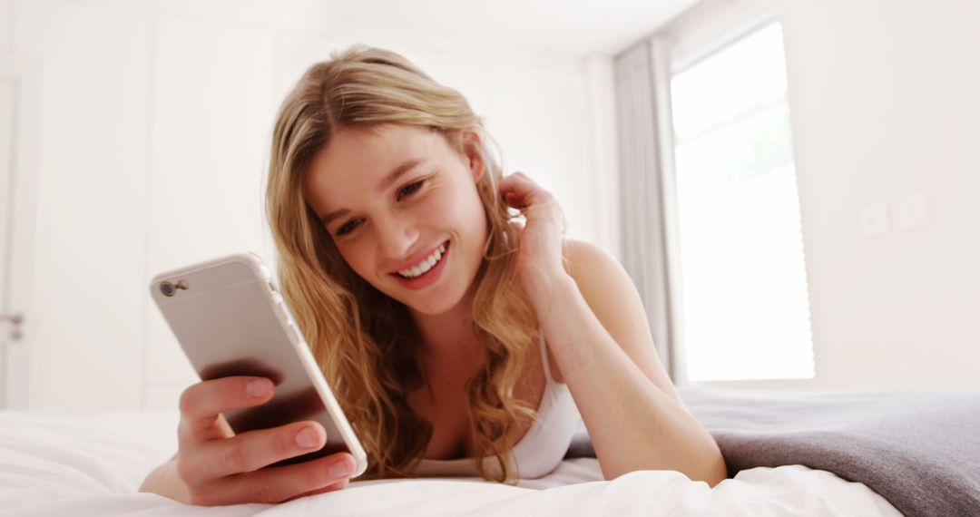 Young Woman Lying on Bed Smiling While Using Smartphone - Free Images, Stock Photos and Pictures on Pikwizard.com