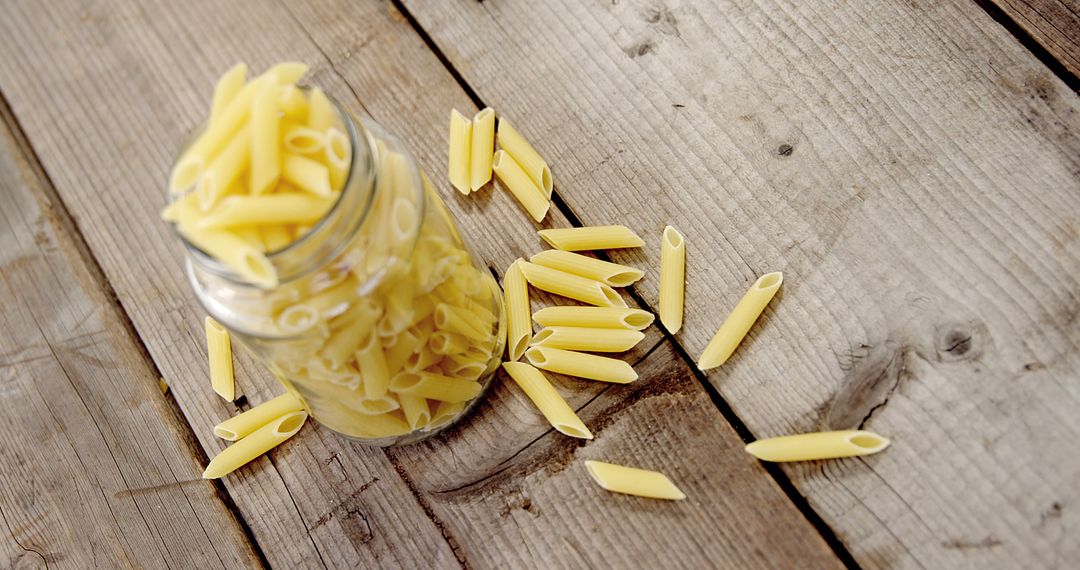 Jar of Dry Penne Pasta Spilling on Rustic Wooden Table - Free Images, Stock Photos and Pictures on Pikwizard.com