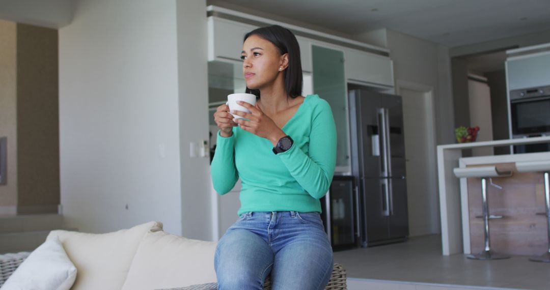 Young Woman Leaning on Sofa with Coffee Cup in Open-Plan Kitchen - Free Images, Stock Photos and Pictures on Pikwizard.com