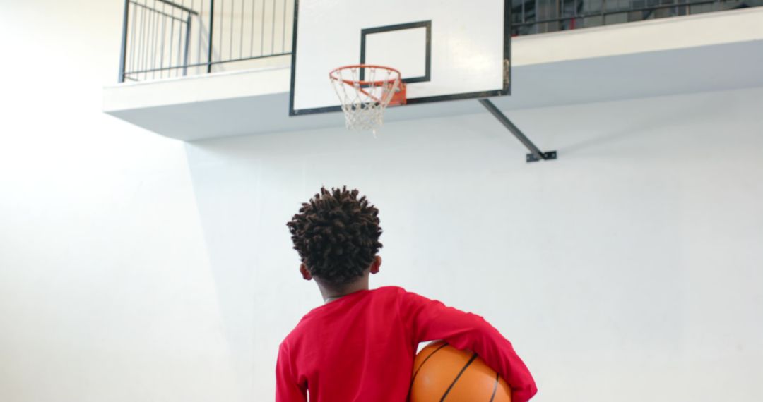 Young Basketball Player Holding Ball Underneath Gym Hoop