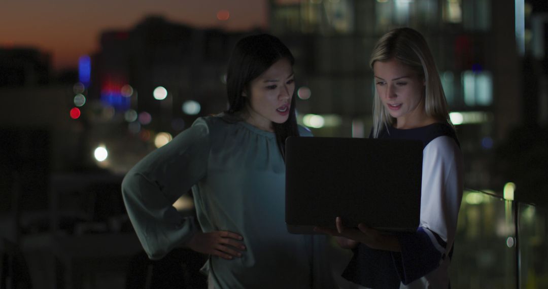 Businesswomen Collaborating on Laptop at Dusk in Modern Cityscape - Free Images, Stock Photos and Pictures on Pikwizard.com