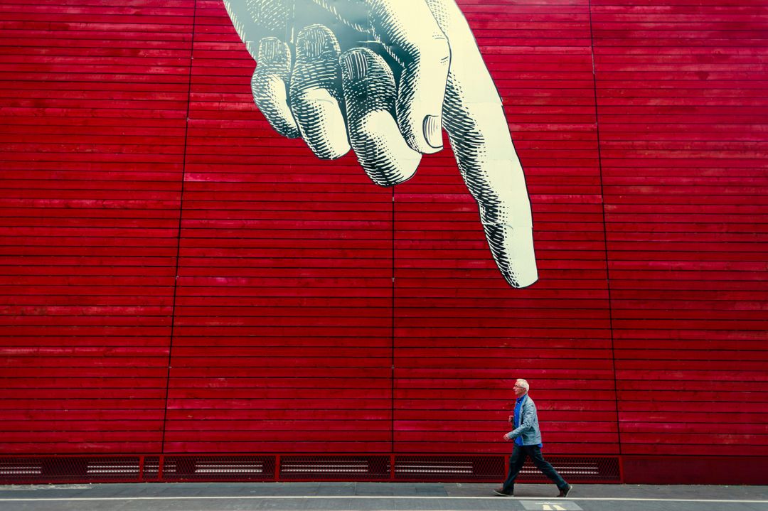 Man Walking Past Red Wall with Artful Giant Finger Pointing Down - Free Images, Stock Photos and Pictures on Pikwizard.com