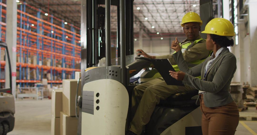 Warehouse supervisor directing forklift operator with clipboard and safety helmets