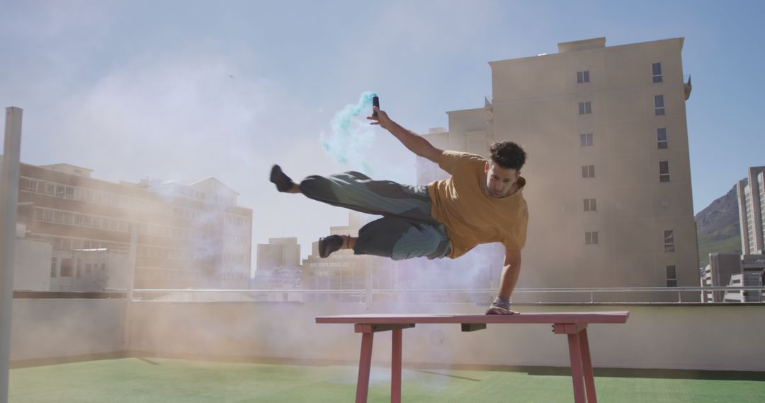 Young man performing parkour trick on rooftop with smoke bomb - Free Images, Stock Photos and Pictures on Pikwizard.com