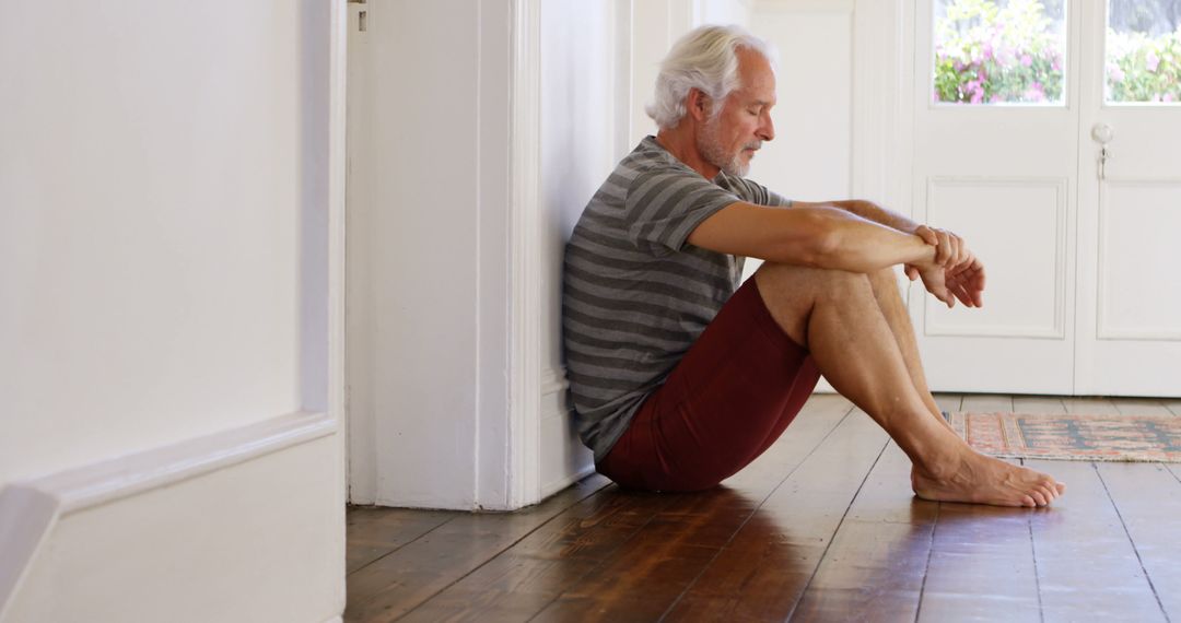 Senior man sitting on hardwood floor looking thoughtful and reflective - Free Images, Stock Photos and Pictures on Pikwizard.com