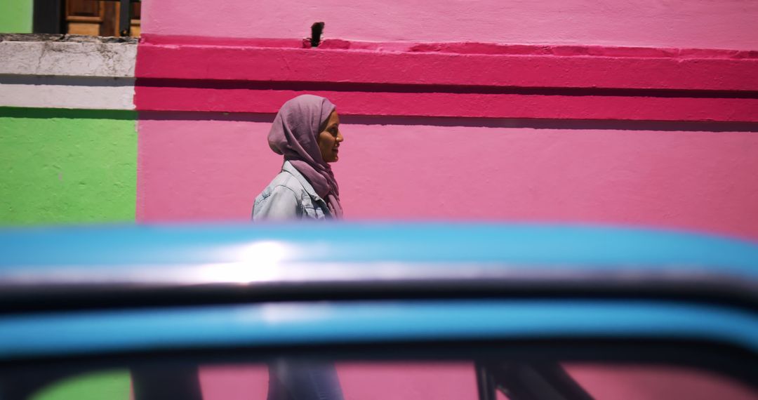 Woman walking past colorful buildings with hijab in urban area - Free Images, Stock Photos and Pictures on Pikwizard.com