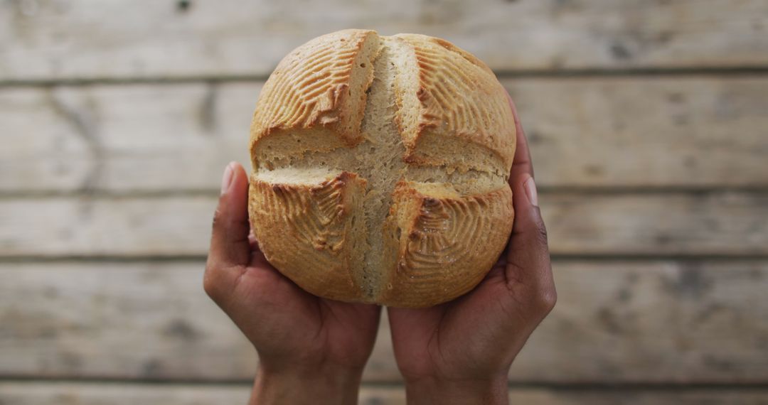 Person Holding Freshly Baked Round Sourdough Bread Over Rustic Table