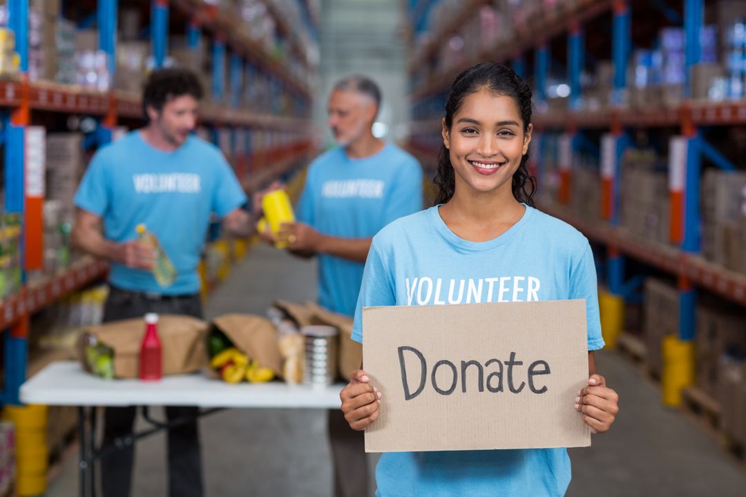 Smiling Volunteer Holding Donate Sign in Warehouse - Free Images, Stock Photos and Pictures on Pikwizard.com
