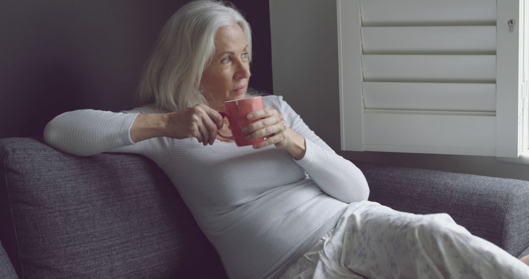 Senior Woman Reflecting While Drinking Coffee on Cozy Couch - Free Images, Stock Photos and Pictures on Pikwizard.com