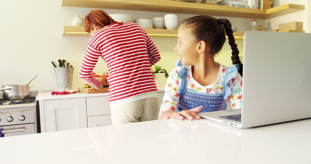 Mother Preparing Food While Daughter Uses Laptop in Kitchen - Free Images, Stock Photos and Pictures on Pikwizard.com