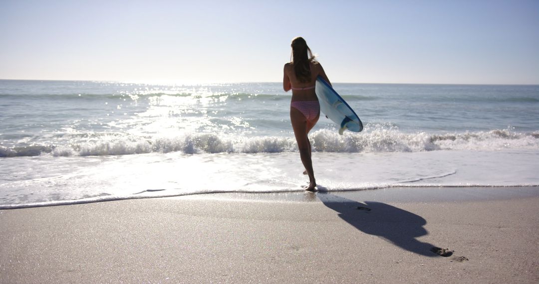 Woman Running Towards Ocean with Surfboard on Sunny Beach