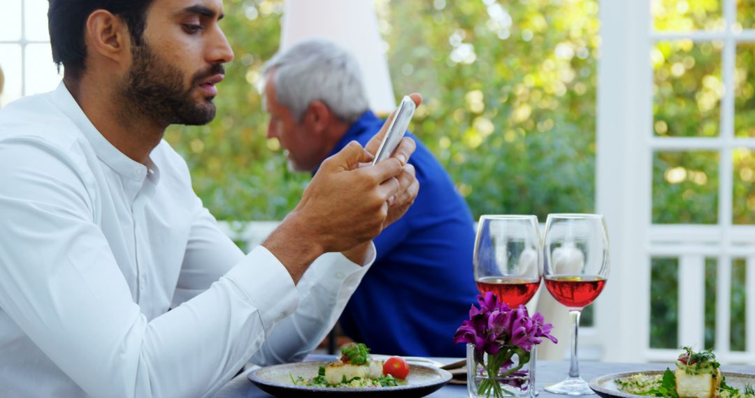 Young Man Using Smartphone at Outdoor Restaurant Table with Wine - Free Images, Stock Photos and Pictures on Pikwizard.com