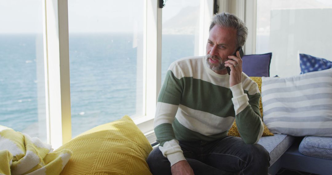 Mature Man Talking on Phone By Ocean View Window - Free Images, Stock Photos and Pictures on Pikwizard.com