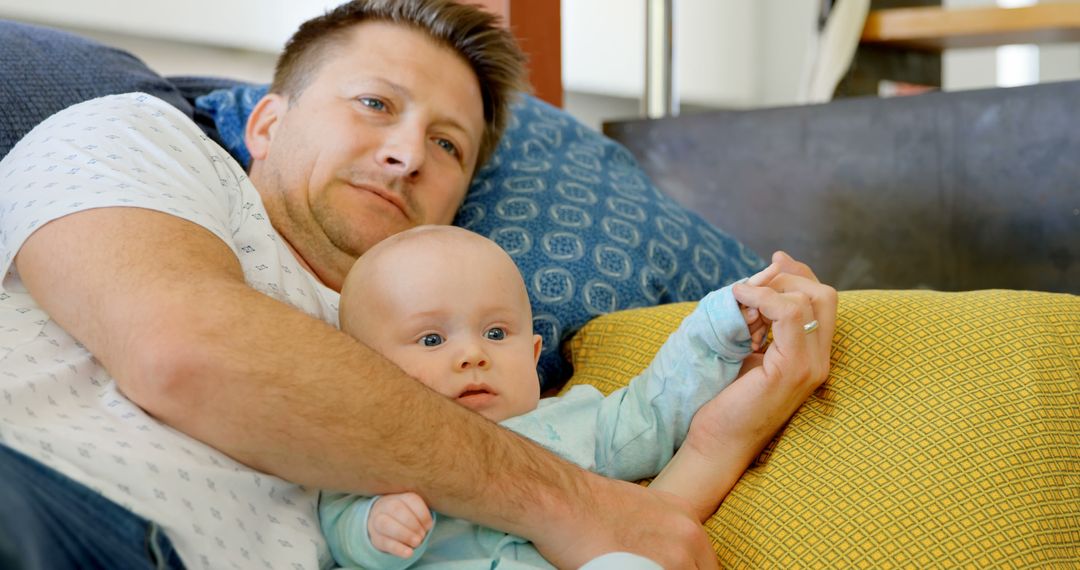 Father Relaxing on Sofa Holding Baby Close During Bonding Time - Free Images, Stock Photos and Pictures on Pikwizard.com