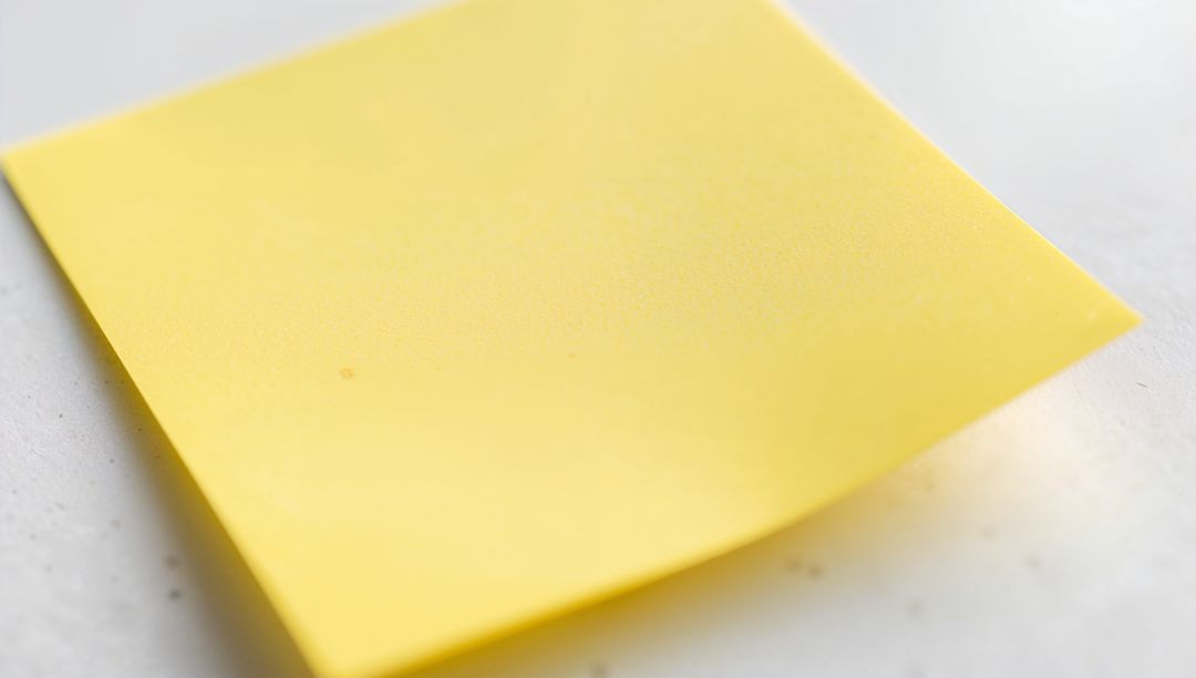Resting Yellow Sticky Note with Curled Corner on Speckled Tabletop