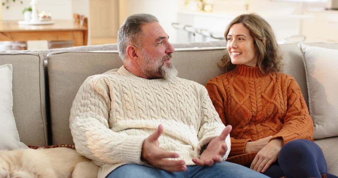 Mature couple relaxing on sofa sharing warm conversation in cozy knit sweaters at home