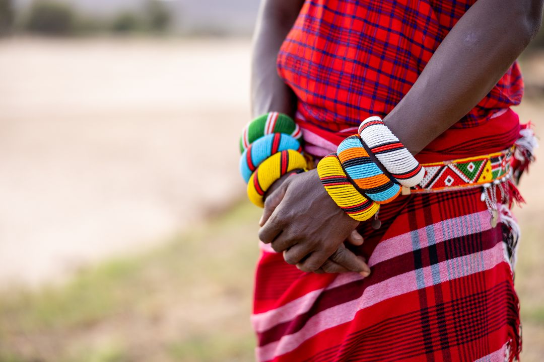 Wearing colorful beaded bangles and red checked wrap, hands clasped showcasing vibrant beadwork