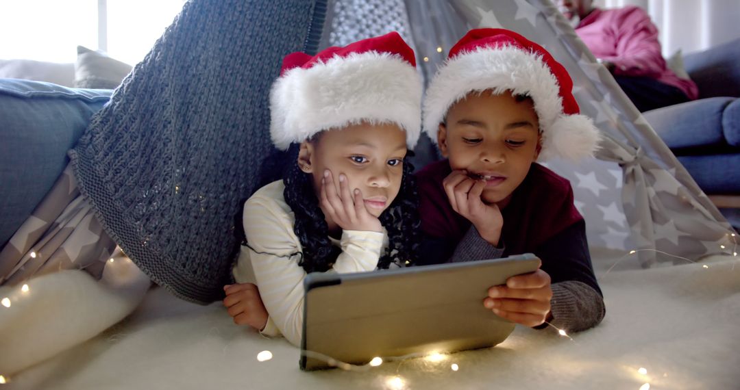 Children in Christmas Hats Using Tablet in Blanket Fort - Free Images, Stock Photos and Pictures on Pikwizard.com