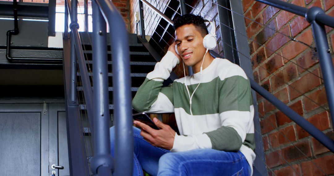 Young Man Listening to Music on Headphones in Stairwell - Free Images, Stock Photos and Pictures on Pikwizard.com