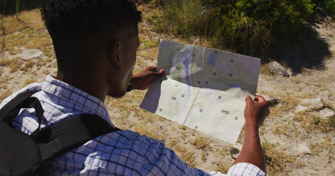 African american man hiking reading a map in coastal countryside - Free Images, Stock Photos and Pictures on Pikwizard.com