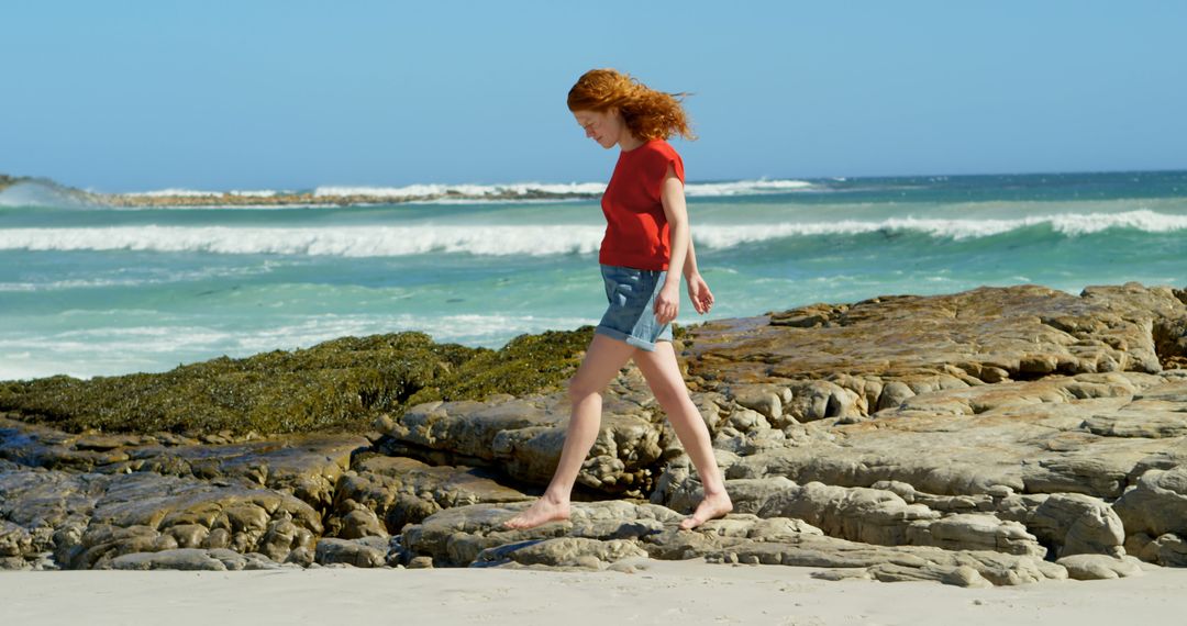 Woman Walking Along Rocky Beach on Sunny Day - Free Images, Stock Photos and Pictures on Pikwizard.com