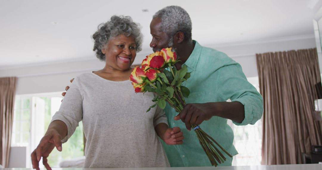 Senior couple in kitchen holding bouquet of flowers and smiling - Free Images, Stock Photos and Pictures on Pikwizard.com