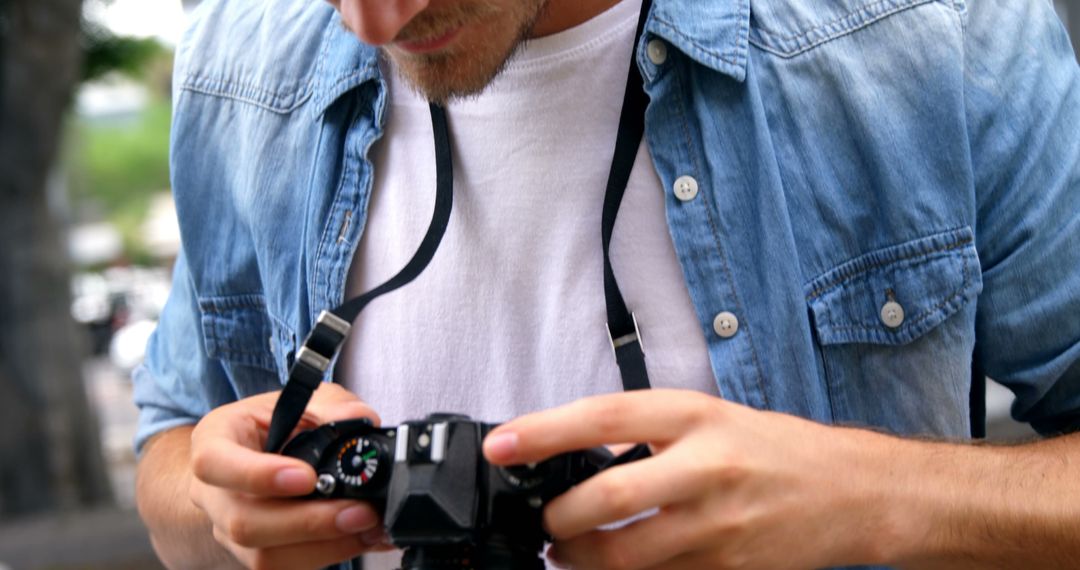 Young Male Photographer Adjusting Camera Settings Outdoors - Free Images, Stock Photos and Pictures on Pikwizard.com