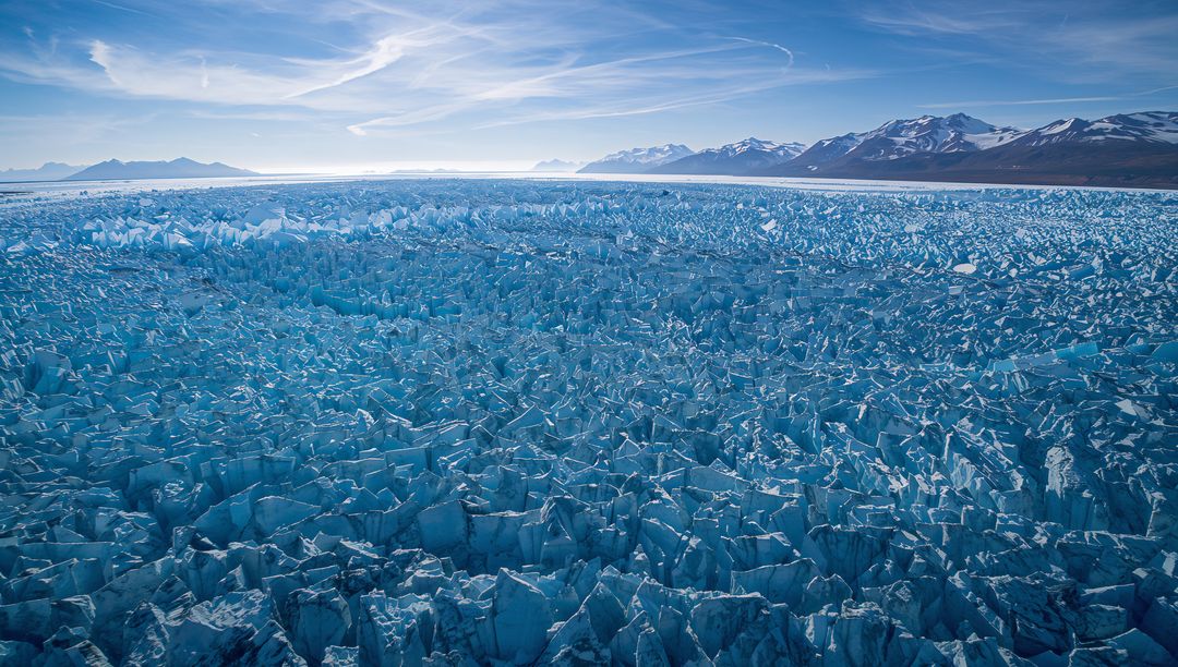 Shimmering glacier field stretching across Arctic coastal plain to snow-capped mountains