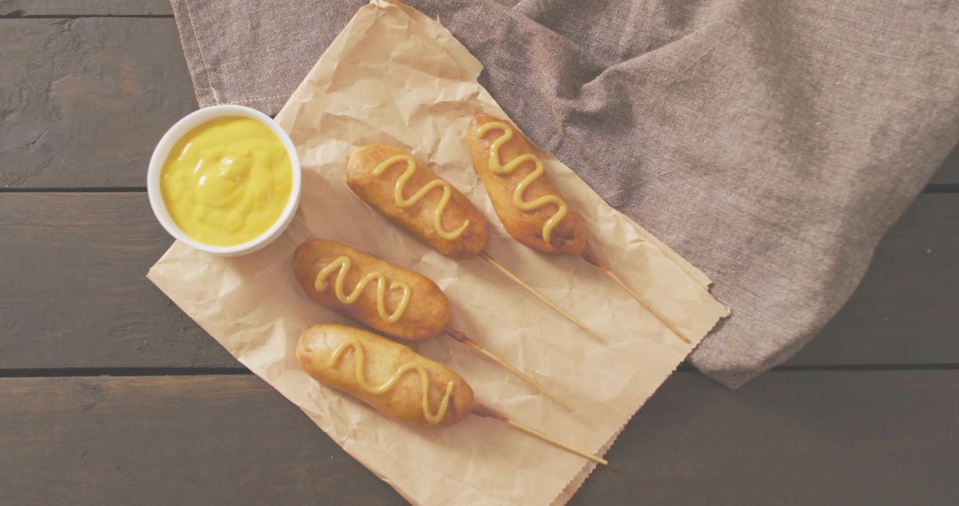 Crispy Corn Dogs on Wooden Skewers Drizzled with Mustard on Rustic Parchment for Party Snack