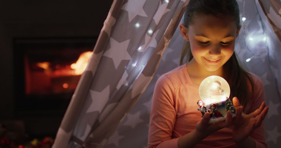 Smiling Girl Holding Glowing Snow Globe Inside Cozy Fort - Free Images, Stock Photos and Pictures on Pikwizard.com