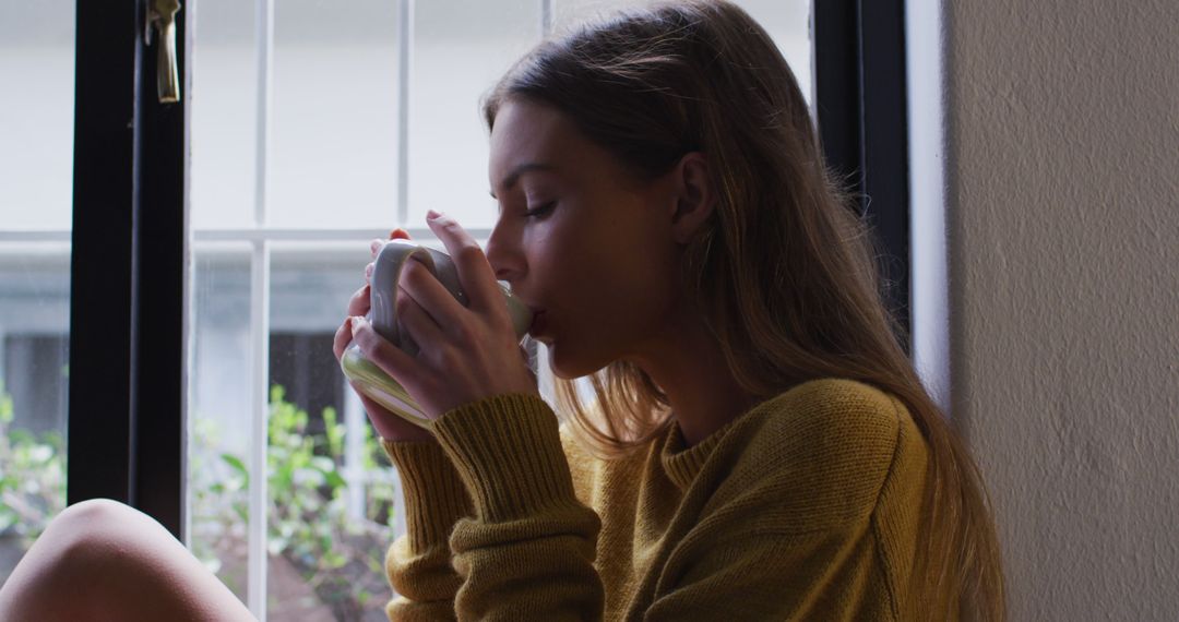 Young Woman Enjoying Warm Beverage Near Window in Cozy Setting - Free Images, Stock Photos and Pictures on Pikwizard.com