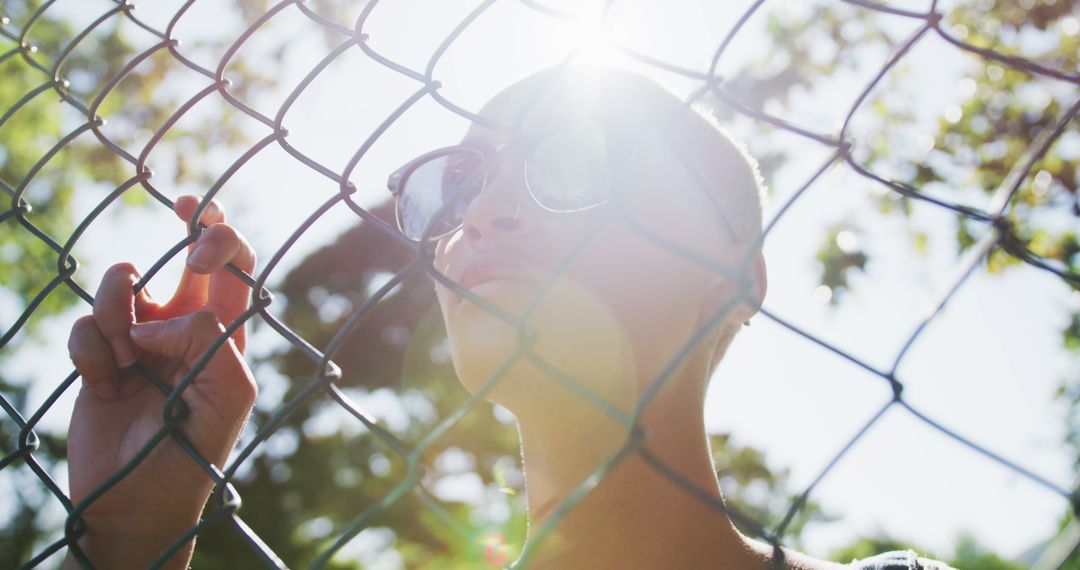 Person Posing Behind Chain Link Fence with Sun Flare - Free Images, Stock Photos and Pictures on Pikwizard.com