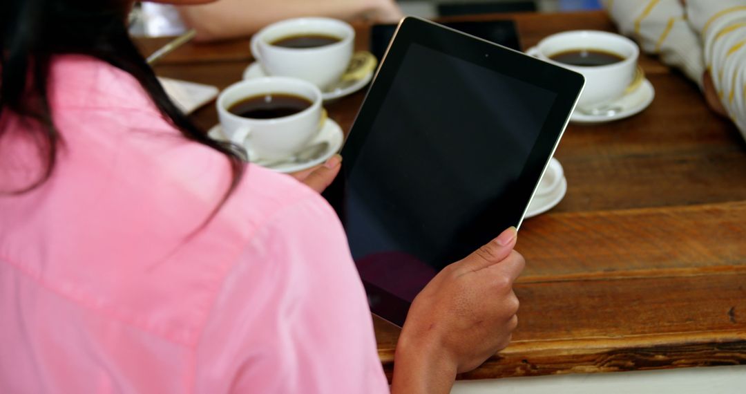 Woman Using Tablet at Cafe with Coffee Cups on Wooden Table - Free Images, Stock Photos and Pictures on Pikwizard.com