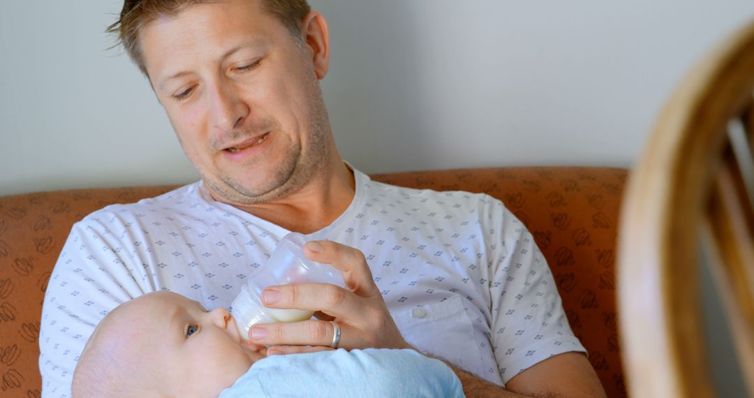 Father Feeding Infant with Bottle While Sitting on Couch - Free Images, Stock Photos and Pictures on Pikwizard.com