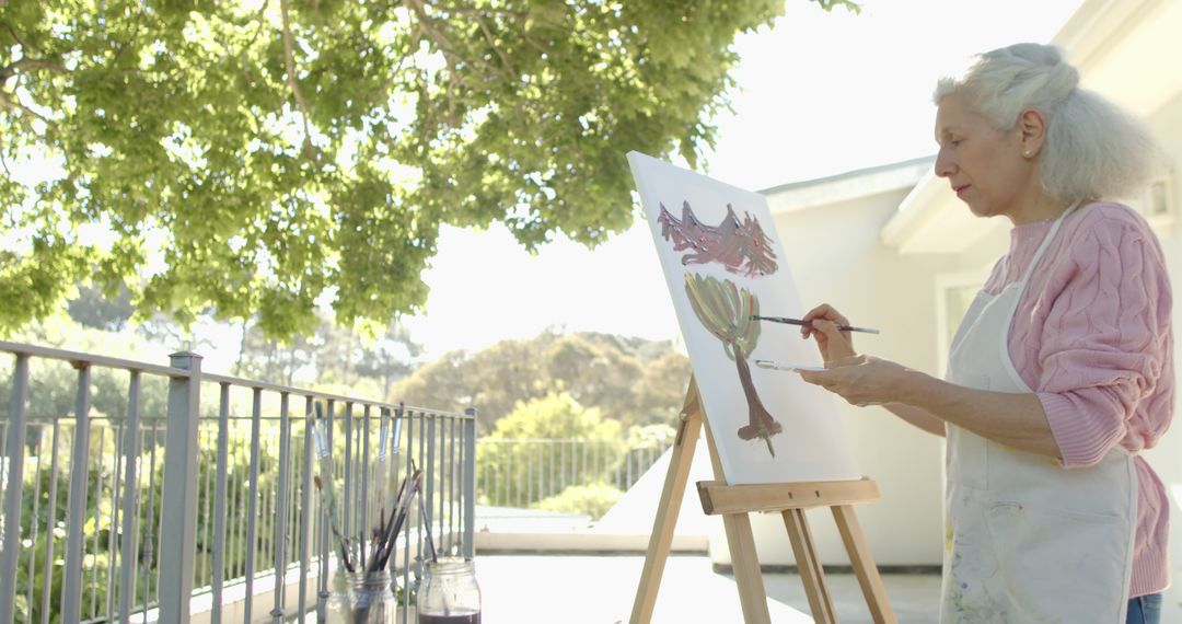 Senior Woman Painting on Canvas in Sunlit Outdoor Patio - Free Images, Stock Photos and Pictures on Pikwizard.com