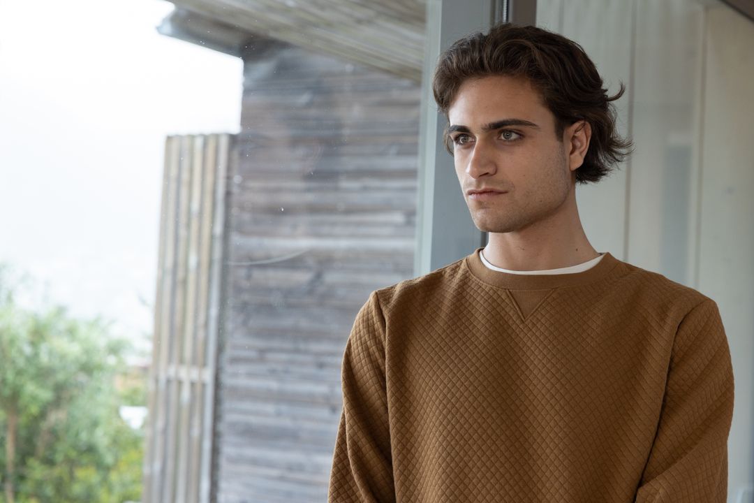 Contemplative Young Man Standing by Window in Modern Home Interior