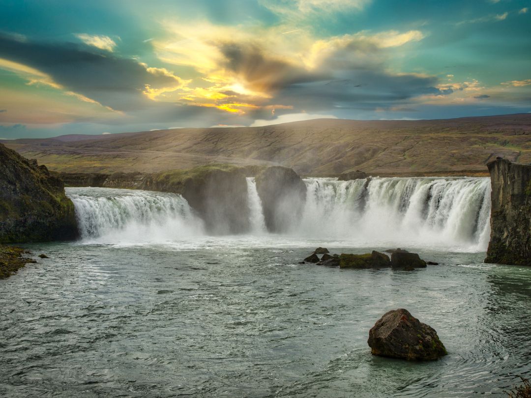 Sunset Glow Over Majestic Waterfall Cascading Into Wide River Across Rugged Highlands