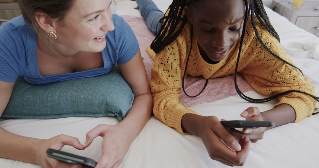 Two Friends Lying on Bed Using Smartphones Smiling - Free Images, Stock Photos and Pictures on Pikwizard.com