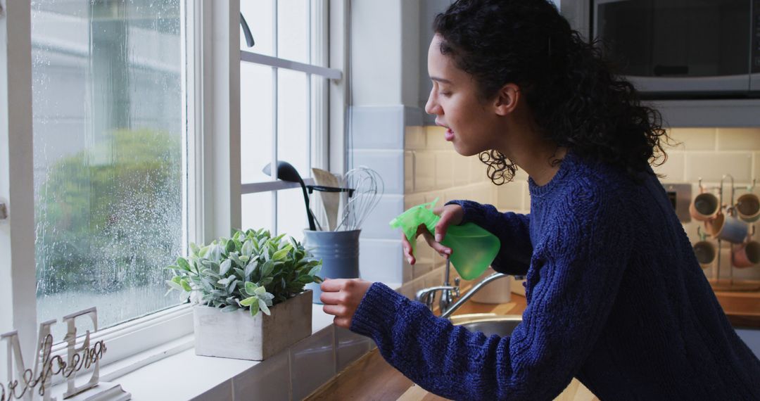 Biracial woman watering plants in kitchen - Free Images, Stock Photos and Pictures on Pikwizard.com