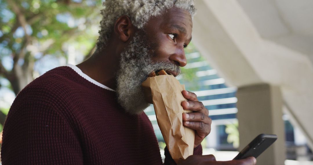 Elderly Man Enjoying Snack While Checking Phone Outdoors - Free Images, Stock Photos and Pictures on Pikwizard.com