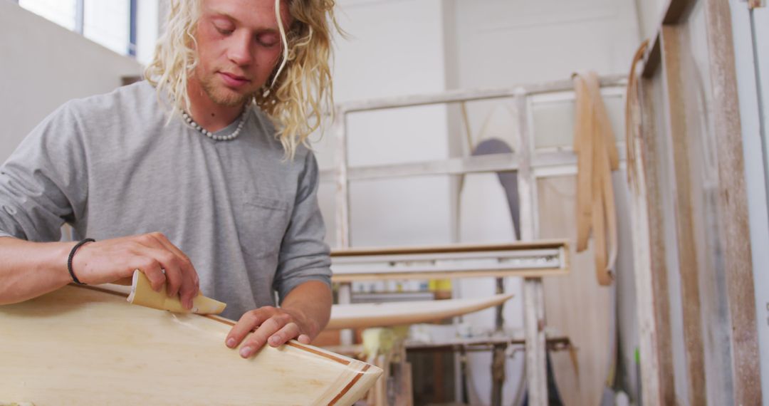 Young Man Shaping Wooden Surfboard in Workshop with Focus and Determination - Free Images, Stock Photos and Pictures on Pikwizard.com