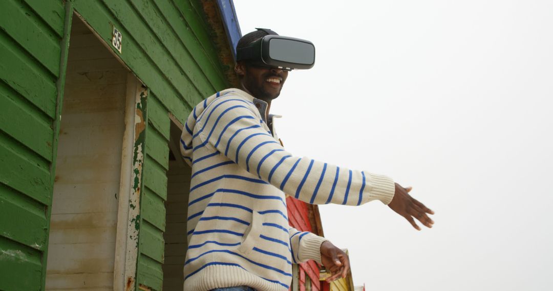 Man Using Virtual Reality Headset Outdoors Near Colorful Beach Hut - Free Images, Stock Photos and Pictures on Pikwizard.com