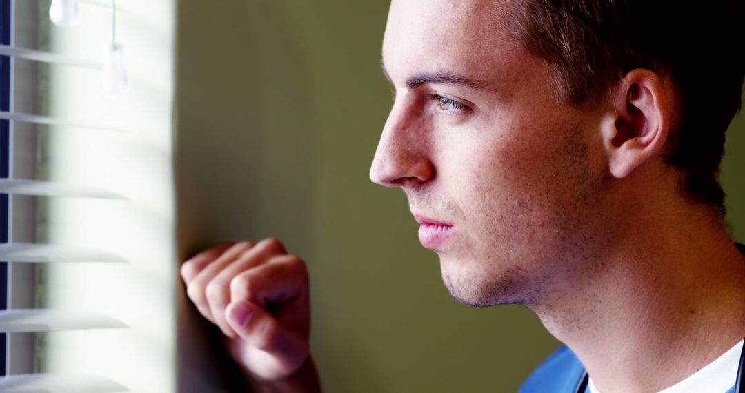 Young Man Looking Through Window Blinds with Pensive Expression - Free Images, Stock Photos and Pictures on Pikwizard.com